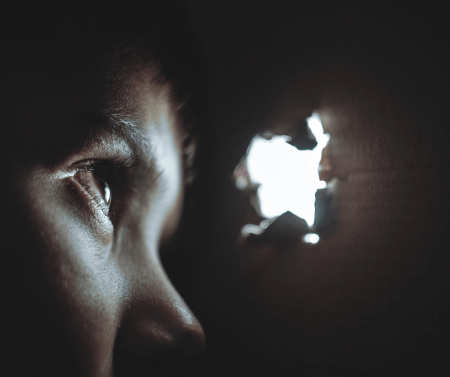 face in the dark looking through a hole